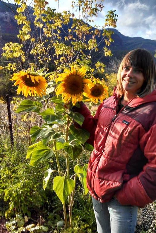 Owner and head microgreen grower is standing next to garden sunflowers.